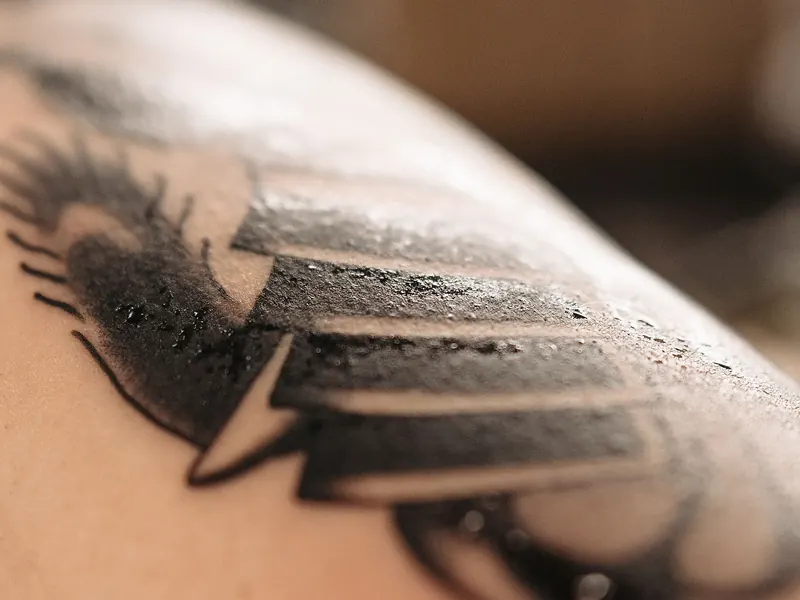 Close-up of a freshly finished black tattoo on a shoulder, the skin still beaded with moisture